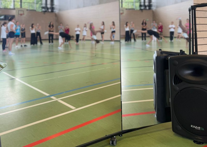 Ein Lautsprecher steht neben einem Spiegel, in der Spiegelung sind Schüler beim Sport in einer Turnhalle zu sehen