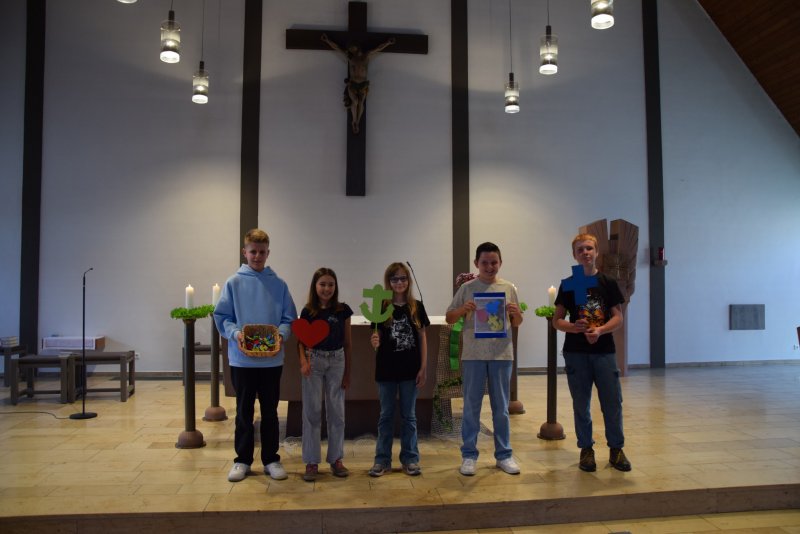 5 Kinder stehen in einer Kirche und halten verschiedene Objekte in die Kamera
