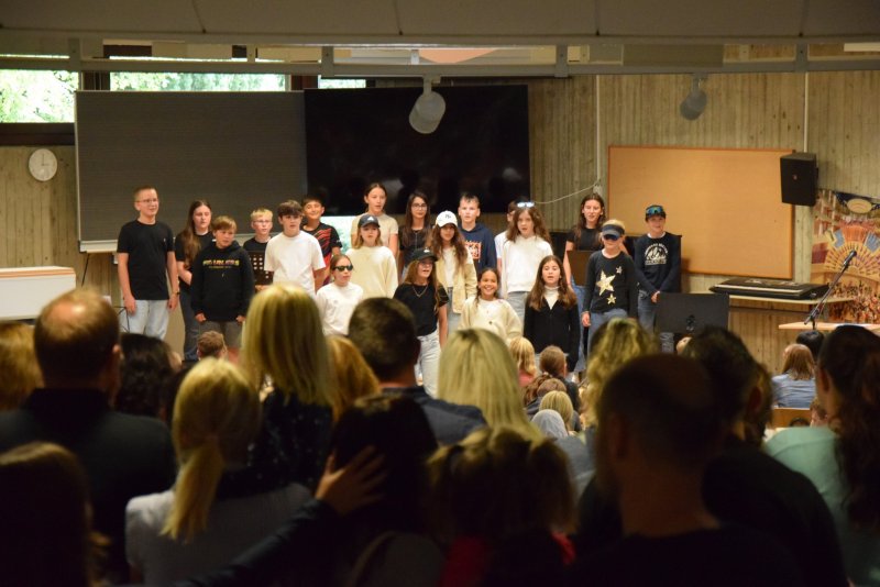 eine gruppe von Kindern steht vor einer Tafel in einem Klassenraum, ein Publikum schaut zu.